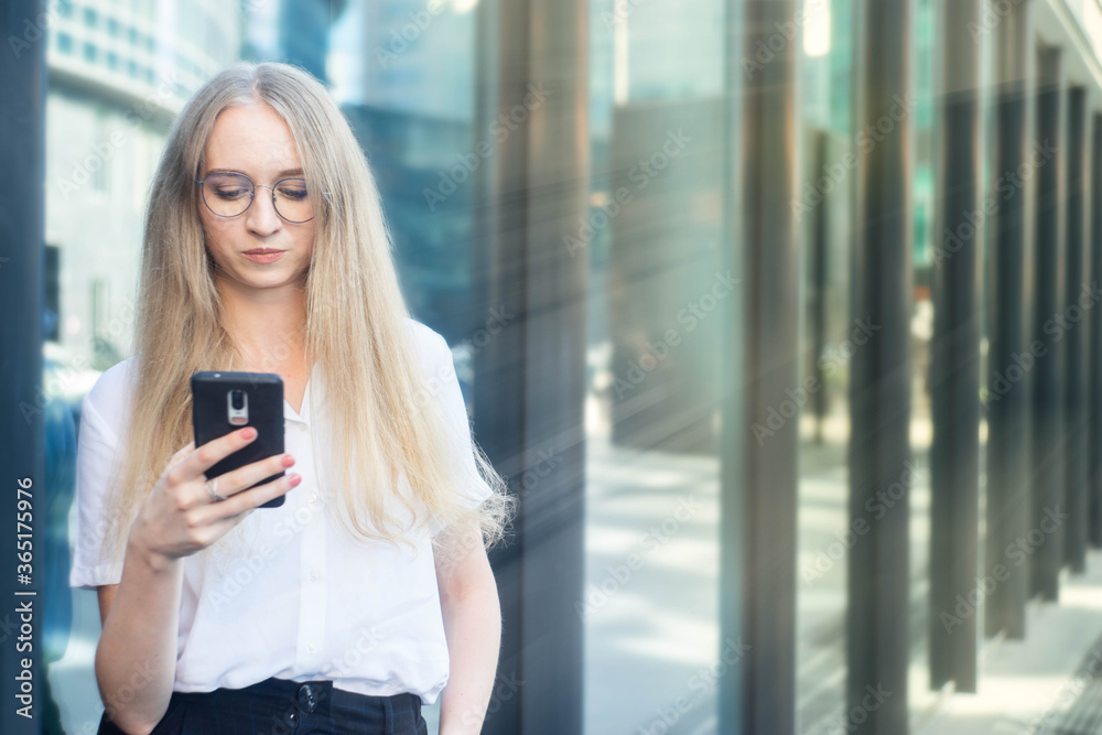 Portrait of a cheerful young caucasian blond business woman holding and looking at phone and thinking.Concept of successful young women in a corporation. Girl in a white shirt. Portrait of a cheerful young caucasian blond business woman holding and looking at phone and thinking.Concept of successful young women in a corporation. Girl in a white shirt.