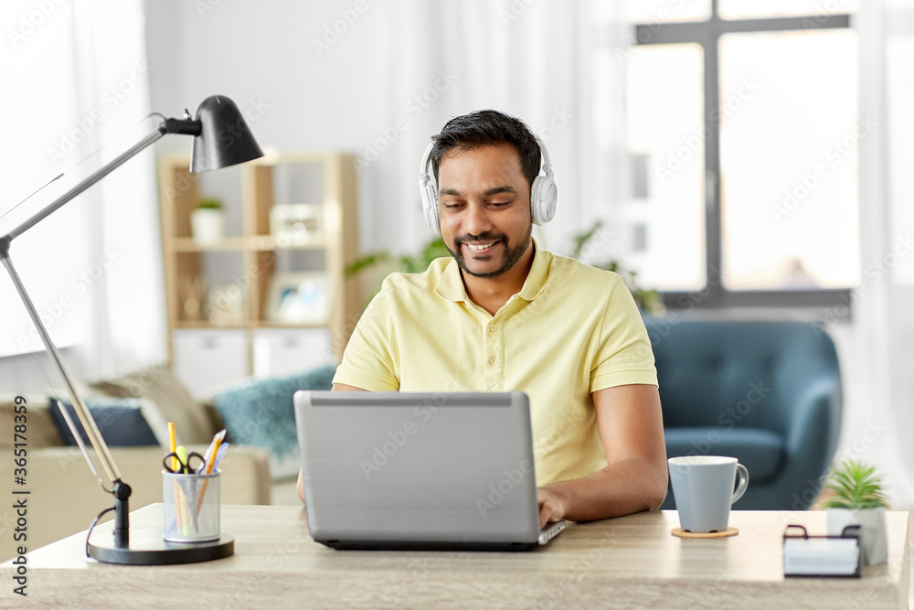remote job, technology and people concept - happy smiling young indian man in headphones with laptop computer working at home office remote job, technology and people concept - happy smiling young indian man in headphones with laptop computer working at home office
