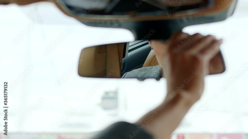 Naklejka premium Serious woman adjusting rear view mirror. Woman sitting behind steering wheel
