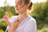 Close-up of face of calm young meditating woman standing on nature with closed eyes holding crossed hands on her chest in yoga posture mudra. Concept of practicing yoga alone outdoor.