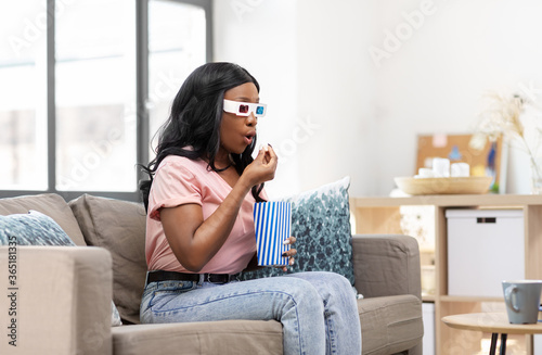 people and leisure concept - surprised african american young woman in 3d glasses watching tv and eating popcorn at home