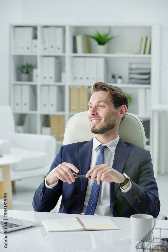 Smiling handsome businessman with stubble sitting at desk and listening to business partner while meeting with him in office Smiling handsome businessman with stubble sitting at desk and listening to business partner while meeting with him in office