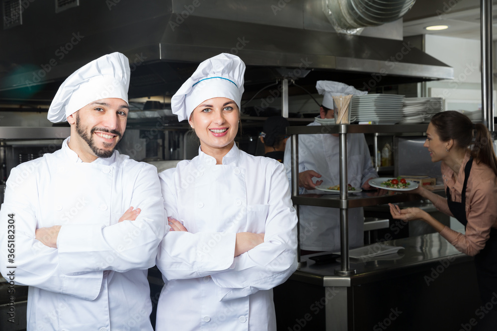 Portrait of two confident chefs posing with crossed arms in professional kitchen