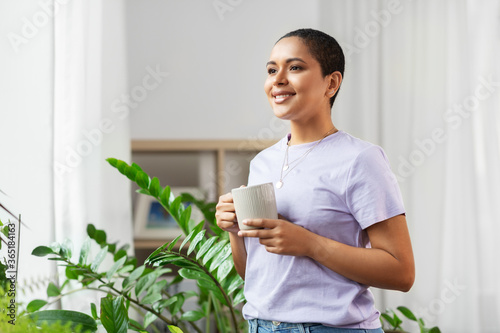people, housekeeping and plants care concept - african american woman with houseplants drinking coffee at home