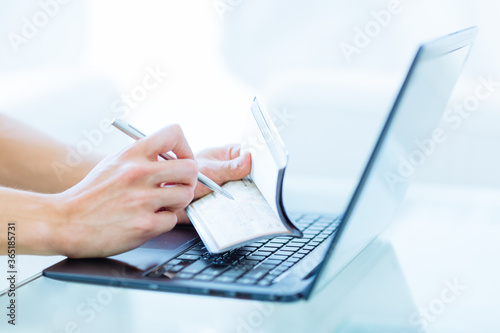 Close-up of a person's hands writing a bank cheque as a money transaction while online on a laptop computer indoors.