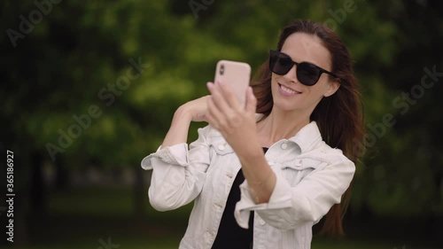 Pretty woman is taking selfie on her cell phone in the park