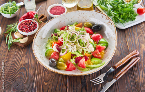 Healthy vegan salad of fresh vegetables - tomatoes, avocado, arugula, olives and slise onion on a bowl with ingredients on wooden backgrouns. Diet food cooking concept