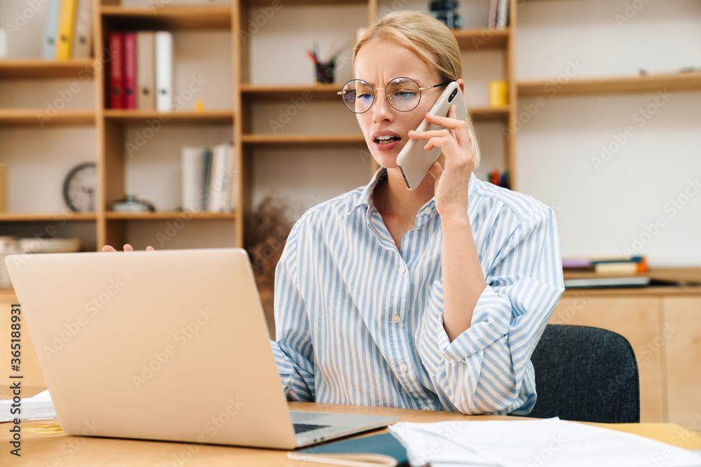 Image of businesswoman talking on cellphone while working with laptop Image of businesswoman talking on cellphone while working with laptop