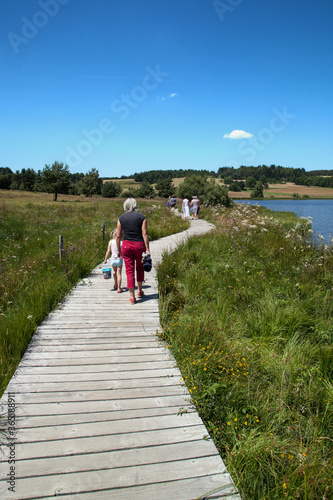 Femme et enfant marchant sur une passerelle en bois au bord du lac de Devesset en Ardèche