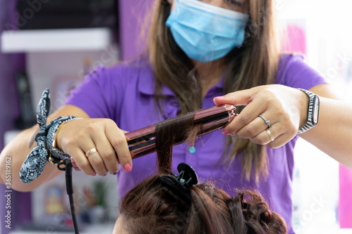 Hairdresser with mask combing a client in her establishment