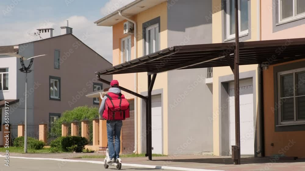 Wide shot of unrecognizable delivery man with red insulated backpack riding electric scooter in suburban area on summer day Wide shot of unrecognizable delivery man with red insulated backpack riding electric scooter in suburban area on summer day