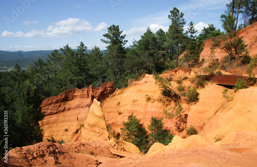 View of colorful orange ochre cliffs with pine trees and blue sky at the natural regional park in Roussillon, Vaucluse, Luberon, France