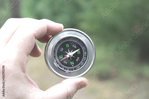 Old classic navigation compass in hand on natural background as symbol of tourism with compass, travel with compass and outdoor activities with compass