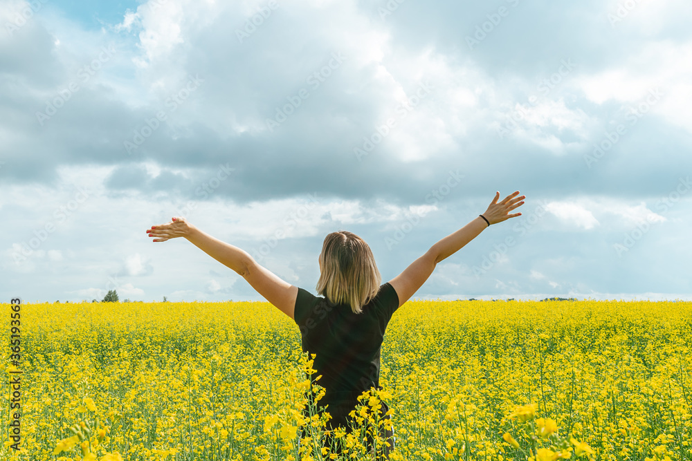 A young woman with raised arms stands in a field with flowering plants summer day. Happiness informative detox concept.