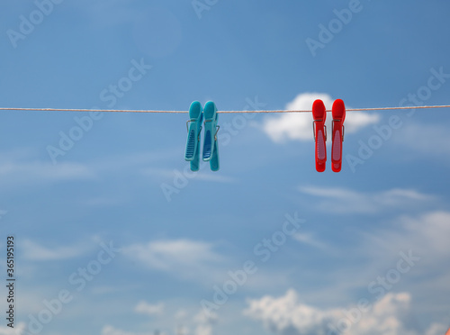 red and blue clothespins on a rope against the background of a bright blue sky with clouds. High quality photo