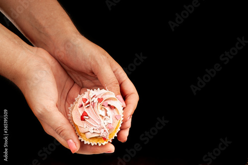 Female hands hold an appetizing  beautiful cupcake on a black background. Unhealthy  sweet food concept