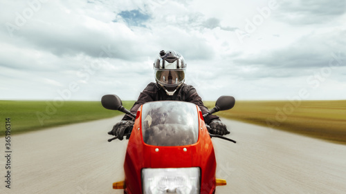 Motorcyclist rides a sports motorcycle at high speed forward, along the highway, looks at the camera