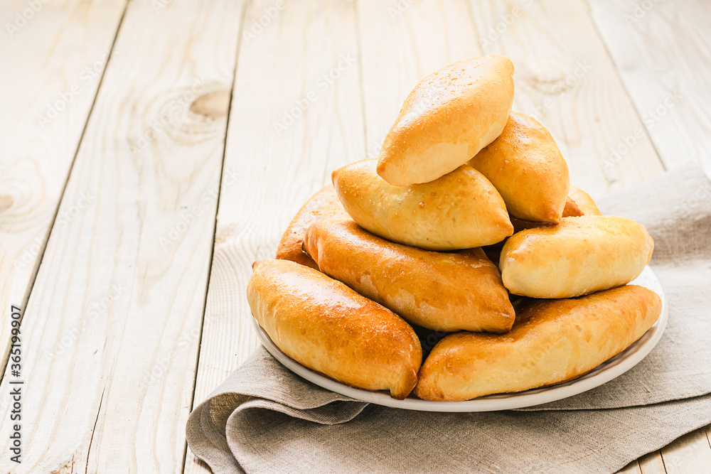 Small portioned pies with a crispy golden crust lie on a plate on a wooden background. Homemade baking concept. Small portioned pies with a crispy golden crust lie on a plate on a wooden background. Homemade baking concept.