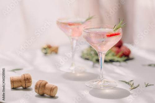Summer drink with white sparkling wine. Homemade refreshing fruit cocktail or punch with champagne, strawberries, ice cubes and rosemary on light background. photo