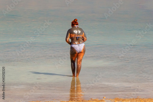 A woman is standing in Dead Sea, turned back, dressed in swim suit and covered with mud in Dead Sea, Jerusalem.