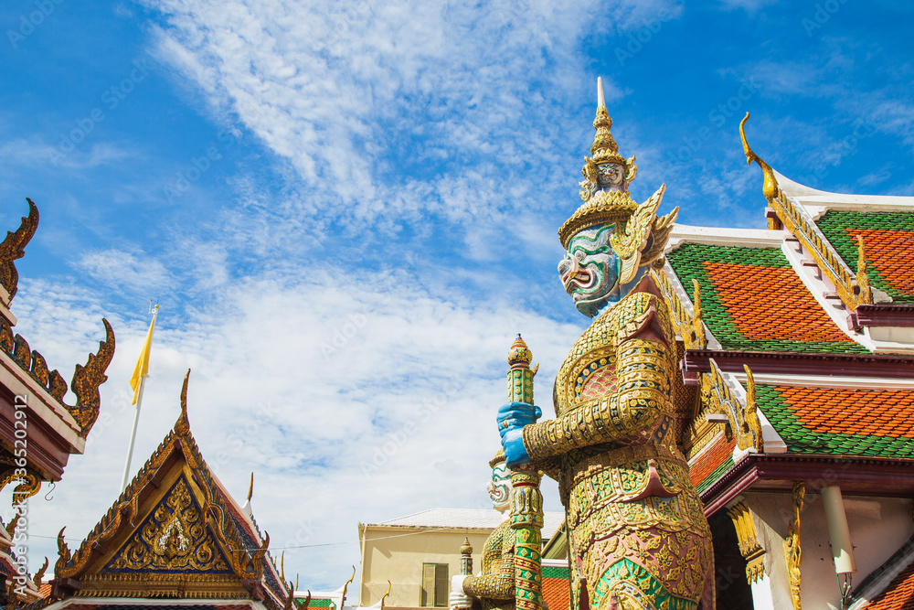 Fototapeta premium A demon guardian statue with a Great golden stupa in Wat Phra Kaew against the sky, Temple of the Emerald Buddha Wat Phra Kaew is one of the most famous places in Bangkok, Thailand