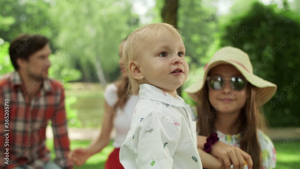 Sister and toddler looking at camera outdoors. Family relaxing together in park Sister and toddler looking at camera outdoors. Family relaxing together in park