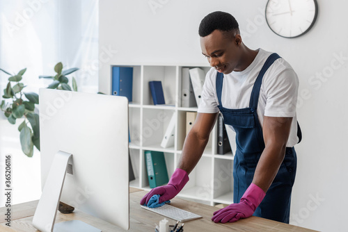 African american worker of cleaning service cleaning computer keyboard with rag in office