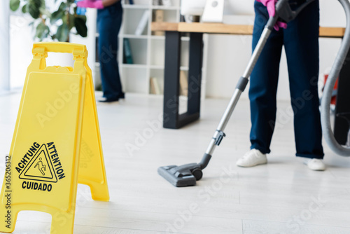 Cropped view of cleaners working in office near wet floor sign with attention lettering on floor