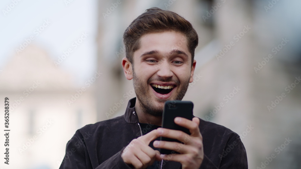 Happy man using phone outside. Surprised guy using cell phone outdoors.