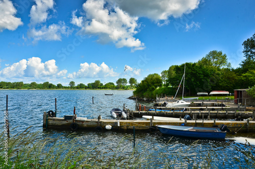 A beautiful coastline at a lake in Germany, Schlei, with a tiny boat at a pier in front of beautiful blue sky and white clouds © Brinja
