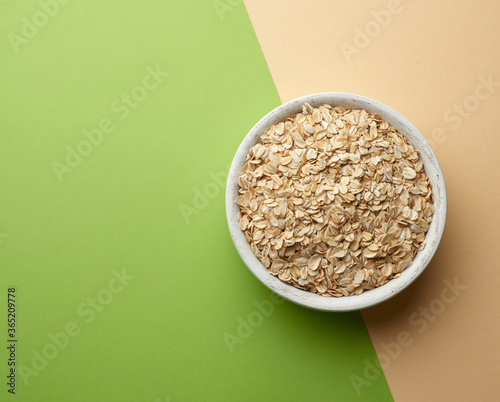 raw oatmeal in a white wooden bowl on a green background photo