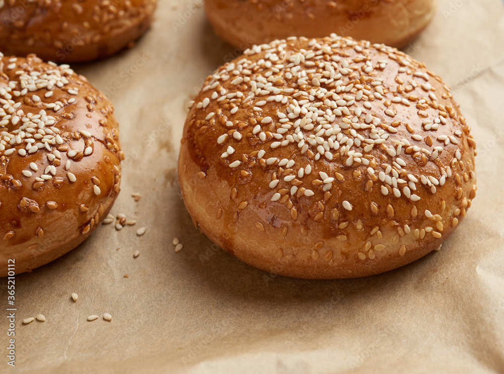 baked sesame buns on brown parchment paper, ingredient for a hamburger