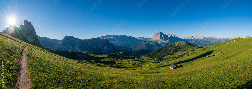 Fototapeta premium Epic mountainlandscape in Puez Odle, Dolomiti / Dolomites Alps in Italy, Seceda area, with Sass Rigais in background, small traditional cottages in green meadow and hiking trail path. Active vacation.
