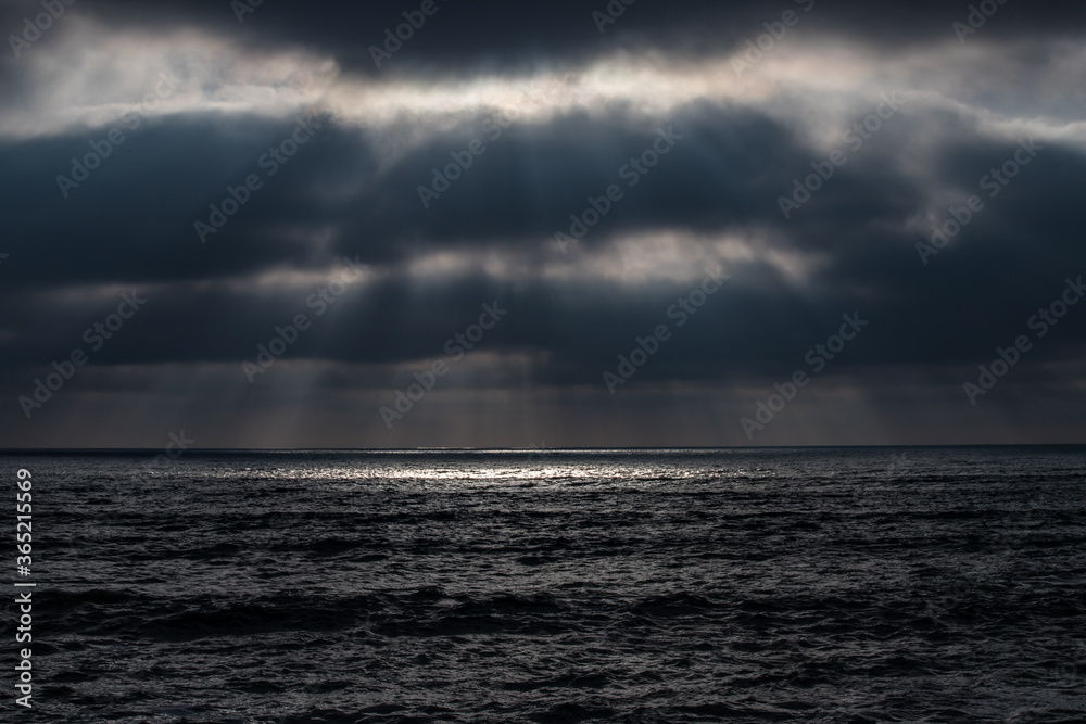 trouées de soleil à travers les nuages noirs qui font des taches sur la mer