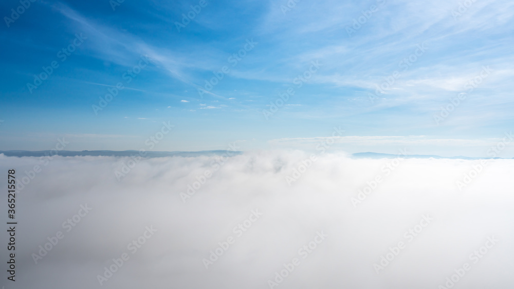 Blue sky above the clouds, small mountains far away