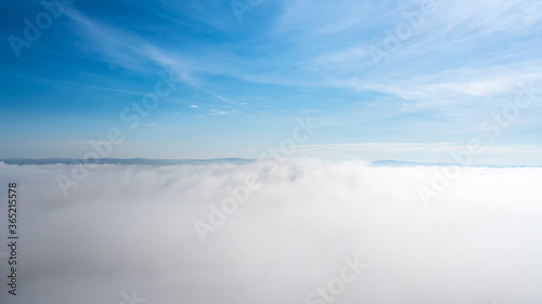 Blue sky above the clouds, small mountains far away
