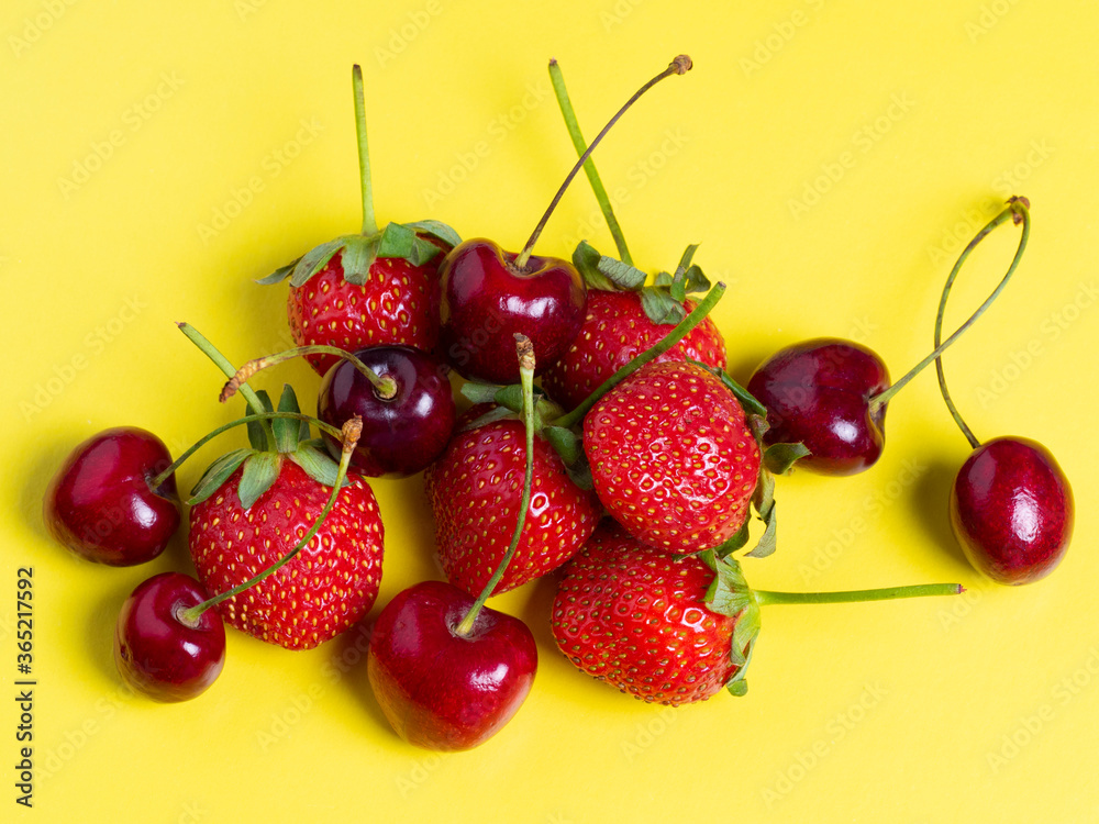 Fresh juicy cherries and strawberries on a bright yellow background. Healthy food, vegetarianism, flat lay