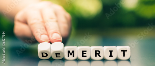 Hand turns dice and changes the word demerit to merit. photo