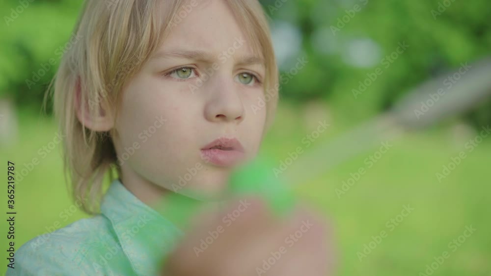 Close-up face of charming blond Caucasian boy blowing soap bubbles outdoors. Portrait of cute little kid having fun in green sunny summer park. Leisure, childhood, joy, lifestyle. Close-up face of charming blond Caucasian boy blowing soap bubbles outdoors. Portrait of cute little kid having fun in green sunny summer park. Leisure, childhood, joy, lifestyle.