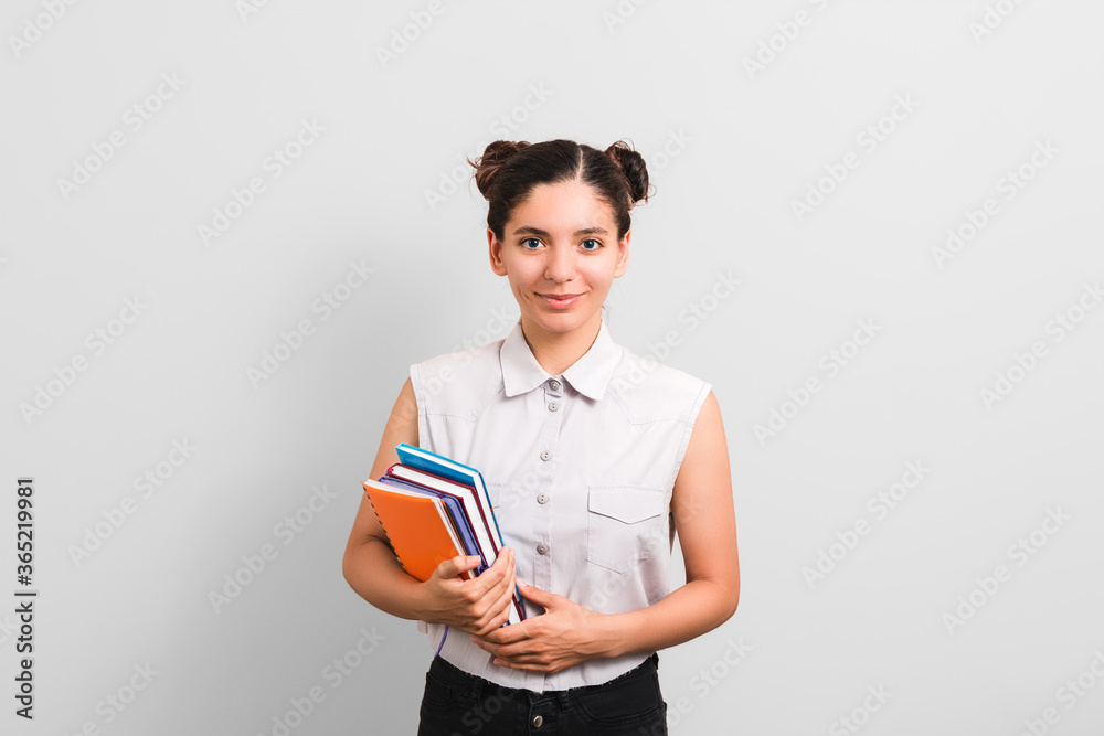 confident young beautiful caucasian female student holding a bunch of notebooks and smiling against grey background. investment in education confident young beautiful caucasian female student holding a bunch of notebooks and smiling against grey background. investment in education