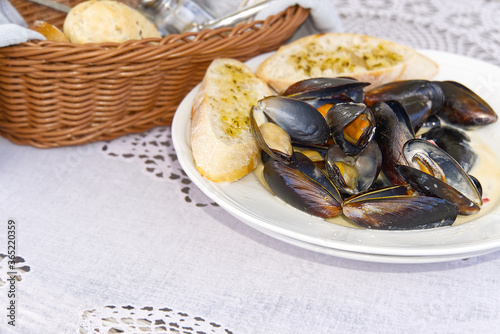 Mussels with white bread on a white plate.