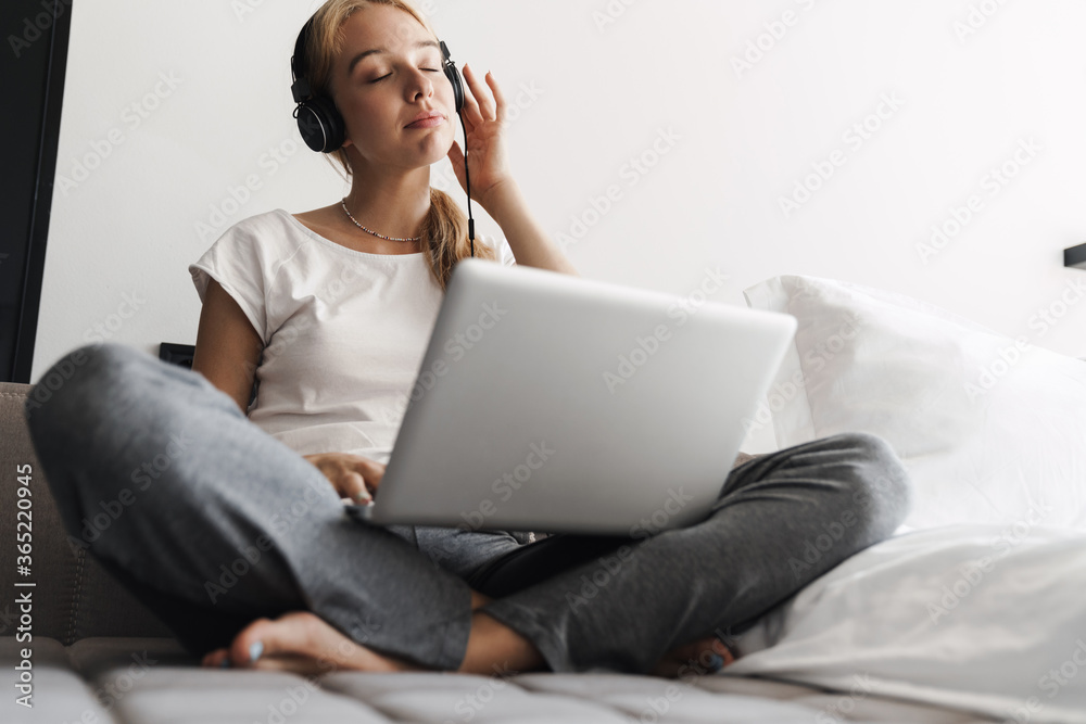 Photo of calm woman using headphones and laptop while sitting on bed Photo of calm woman using headphones and laptop while sitting on bed