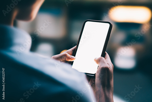 Woman's hands holding mobile phone with lighted big copy space touch screen outdoors with evening bokeh light of city. Close up view of female person using smartphone app for online shopping