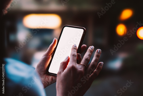 Woman's hands holding mobile phone with big copy space touch screen outdoors with evening bokeh light of city on background. Close up view of female person using smartphone app for online shopping