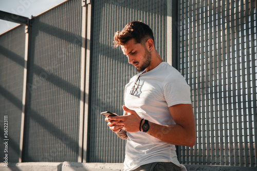 Ragazzo giovane e attraente scrive messaggi con il suo cellulare mentre si trova in una località metropolitana photo