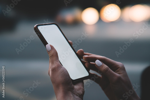 Cropped view of woman's hands holding modern smartphone device with blank screen area for your internet content or website on bokeh background.Digital mobile phone with mock up area