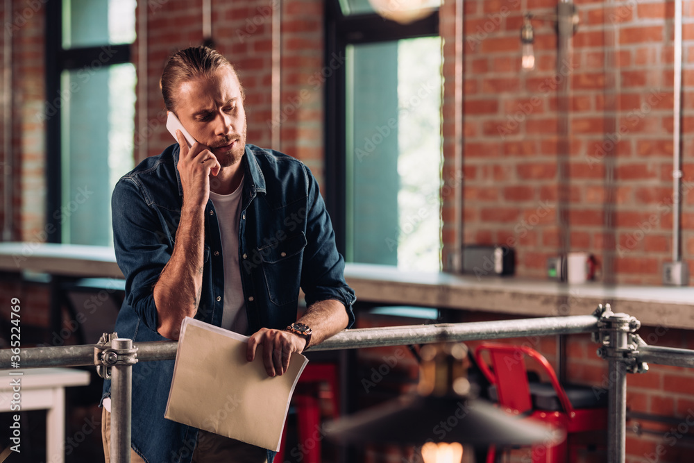 Fototapeta premium selective focus of bearded businessman talking on smartphone and holding folder in office