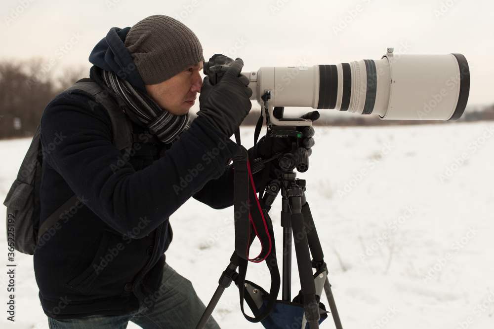Photographer in winter with big zoom lens on the tripod 