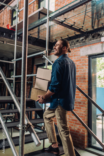 selective focus of smiling businessman holding boxes while walking on stairs in office