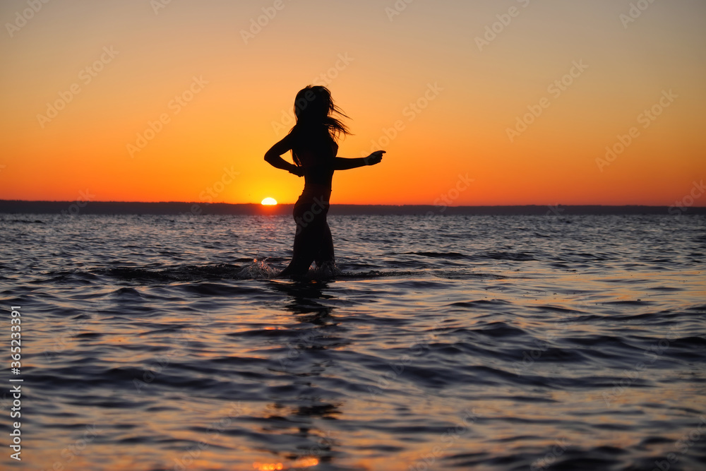 The girl swims in the sea, splashes in the water at sunset. Relaxation and happy pastime. Summer vacations.